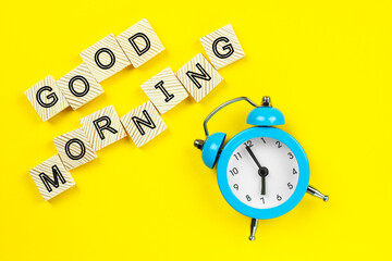 good morning inscription from wooden cubes and alarm clock, on a yellow background