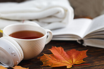 A Cup of hot coffee or tea with autumn leaves and headphones on a brown wooden background