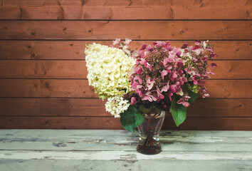 Autumnal fading pink and white hydrangea flowers in glass vase. Toned image. View with copy space.