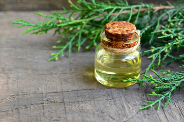 Juniper essential oil in a glass bottle on old wooden background. Herbal medicine, spa, aromatherapy and body care concept wit copy space.Selective focus.