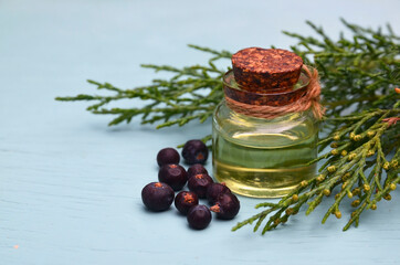 Juniper essential oil in a glass bottle on a blue wooden background. Herbal medicine, spa, aromatherapy and body care concept wit copy space.Selective focus.