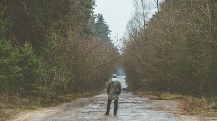 Rear view of a men in a warm jacket and knitted hat standing in a misty forest