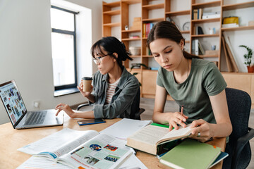 Fototapeta na wymiar Image of nice multinational student girls doing homework with laptop