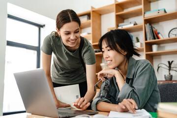 Obraz premium Image of smiling multinational student girls doing homework with laptop