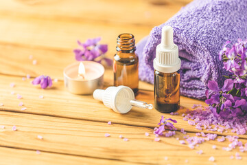 Spa still life with violet oil, violaceous bath salt in glass jar and perfumed candle on natural wood table surface.