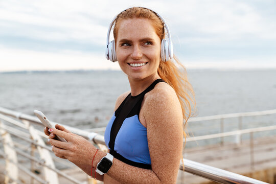 Image of redhead happy sportswoman using cellphone while working out