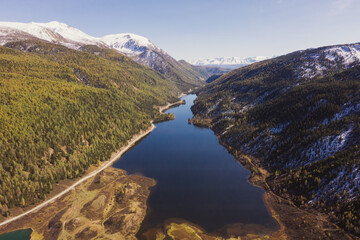 Fototapeta premium Colourful mountains valley, blue snow covered peaks, orange and green autumn forest and mountain lake. Aerial view