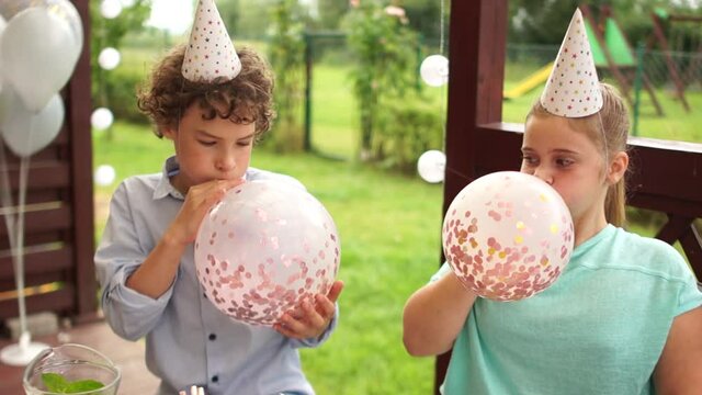 Teenagers in birthday hats oy and girl at the birthday party have fun stuffing big balloons with sparkles inside. Happy childhood