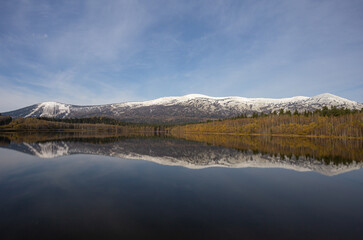 view of the ski resort in autumn. a mountain range covered with snow with ski slopes is reflected in the surface of a large lake