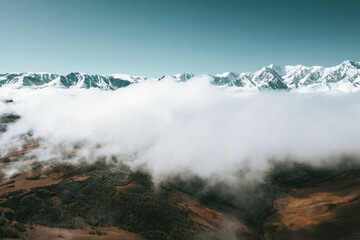 Aerial drone view above clouds on mountains landscape  with snow peaks and fur forests