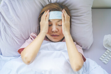 Sick asian woman lying on bed have fever and using a cooling pad on head. © Pormezz