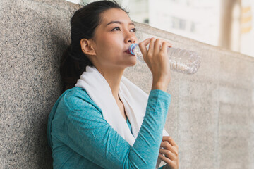 Asian woman drinking water to rehydrate to avoid heat stroke after running outdoors in the summer.