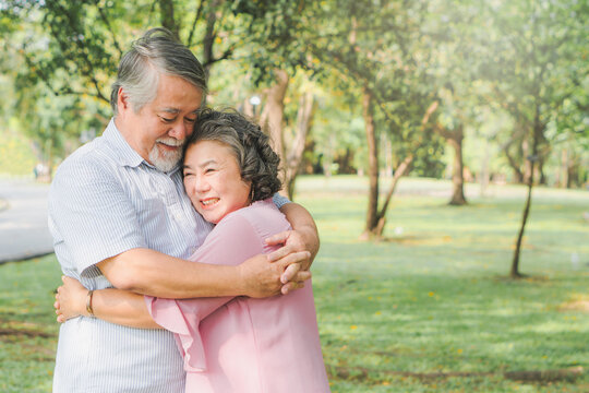 Happy asian elderly couple hugging together in the park