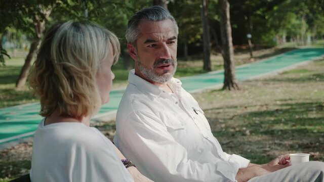 Elderly man and woman Sitting talk in garden during summer morning. Senior Couple come for long weekend for picnic at park. Health care Living retire of old people. International Day of Older Persons