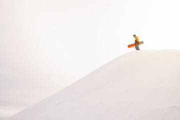 Naklejka na ściany i meble Snowboarder standing on a slope holding board. White snow background