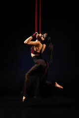 Brunette beautiful caucasian woman in Lace mask doing circus tricks on red silks isolated on black background.