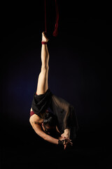 Brunette beautiful caucasian woman in Lace mask doing circus tricks on red silks isolated on black background.
