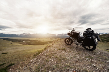 Motorcycle with trunks and bags on a long journey standing on the cliff in mountains landscape. Altai mountain