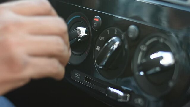 Close up shot of a hand turning the fan knob of the air conditioning in a vehicle, then pressing the car stereo volume button