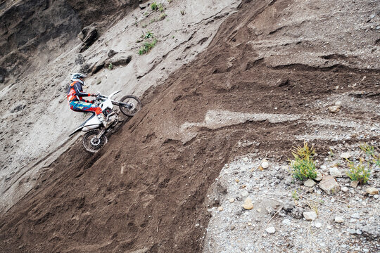 Rider climbing sand quarry mountain on off-road enduro motorcycle