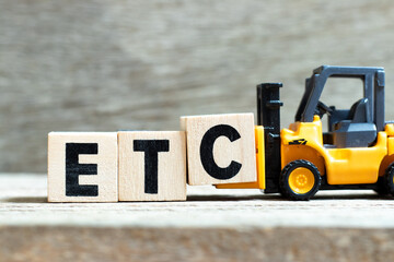 Toy forklift hold letter block c to complete word etc (abbreviation of et cetera) on wood background