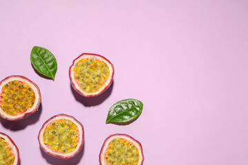 Halves of passion fruits (maracuyas) and green leaves on pink background, flat lay. Space for text