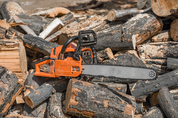 Chainsaw that stands on a heap of firewood in the yard on a background of firewood and trees cut by a chainsaw