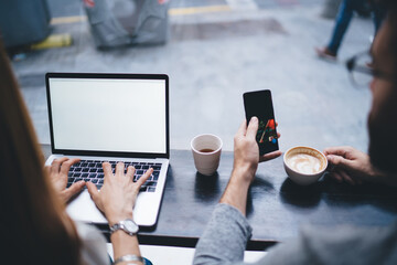 Unrecognizable couple of freelancers with laptop and smartphone drinking coffee