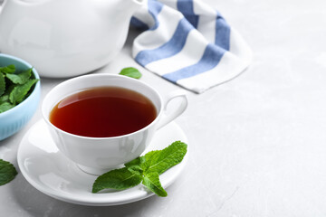 Cup with hot aromatic mint tea on light table, space for text