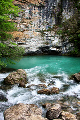Fototapeta na wymiar Mountain emerald lake with big rocks and cliff behind, closeup