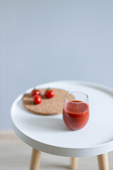 Ripe mini tomatoes with a glass of tomato juice on a white table. Vertical orientation