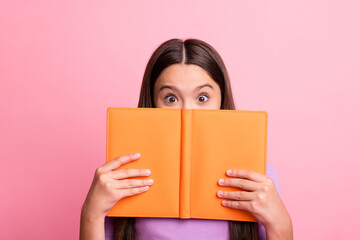 Photo of excited impressed kid girl hide her lips with book wear violet jumper isolated over pastel...