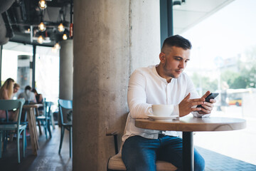 Naklejka na ściany i meble Focused man surfing internet on smartphone in cafe