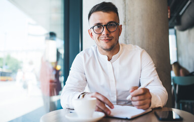 Smiling man in eyeglasses with coffee and notebook in cafe