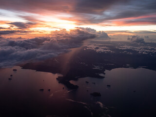 aerial view of sunset from aircraft window seat. broken cloud overcast the terrain. flying along the coast. rain precipitation from cloud falling into earth.