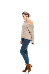 full length view of fashionable woman in openwork sweater and jeans posing on white