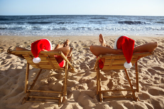 Lovely couple with Santa hats relaxing on deck chairs at beach, back view. Christmas vacation