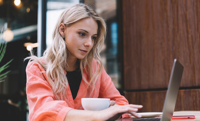 Young caucasian female millennial typing on laptop computer searching information and reading news,...