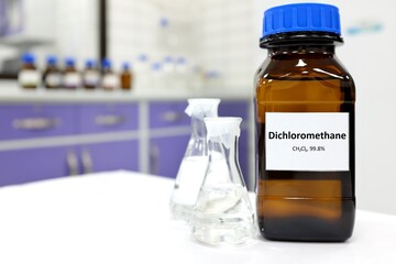 Selective focus of dichloromethane liquid chemical compound in dark glass bottle inside a chemistry laboratory with copy space.