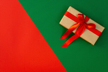 Christmas minimal composition. Gift craft box with a satin bow, decorations on a red-green background. Flat lay, top view, copy space.