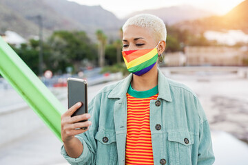 Trendy hipster latin woman wearing colorful face mask and looking at her smartphone