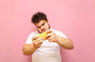 Portrait funny overweight gamer standing on a pink background and playing mobile games on a...
