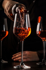 Sommelier pouring rose wine into glass at wine tasting in winery, bar or restaurant. Dark background