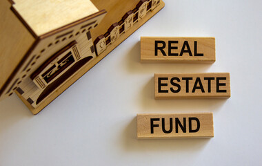 Wooden blocks form the words 'real estate fund' near miniature house. White background. Business concept, copy space.