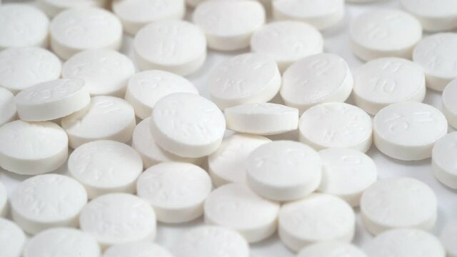 Slow rotation of a large group of white pills on a white background and one yellow pill on the middle. A medicine concept. Close up shot with selective focus