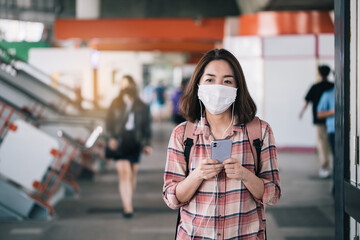 Fototapeta na wymiar Asian woman wearing surgical face mask against novel coronavirus or corona virus disease (Covid-19) at public train station. Relax and listening music on the way.