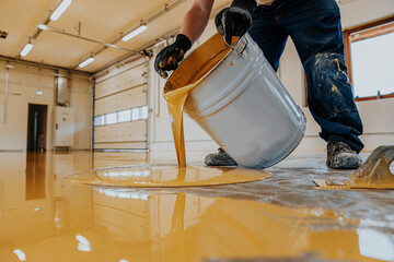 Worker applying a yellow epoxy resin bucket on floor. - obrazy, fototapety, plakaty