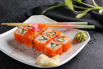 Japanese cuisine. Rice rolls with red caviar and wasabi on a white plate on a black table with chopsticks. Restaurant menu. Background image, copy space