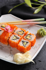 Japanese cuisine. Rice rolls with red caviar and wasabi on a white plate on a black table with chopsticks. Restaurant menu. Background image, copy space