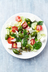 Healthy Salad with Feta Cheese, Green Olives, Baby Spinach, Cucumber, Cherry Tomatoes and Capers. Bright wooden background. Top view. Close up.